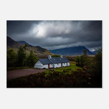 Blackrock Cottage Glencoe wall art showing a dark moody wide view of the white cottage surrounded by rough moorland and dramatic Scottish mountains under heavy clouds