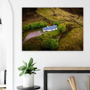 Blackrock Cottage Glencoe wall art showing an aerial view of the long white cottage with red doors surrounded by green moorland, trees and winding tracks