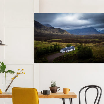 Blackrock Cottage Buachaille Etive Mòr wall art showing the white cottage in front of a dramatic Scottish Highlands mountain under dark storm clouds and moody light