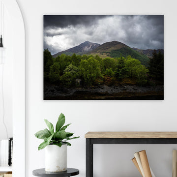 Glencoe and Glen Etive wall art showing bright green trees in front of rocky Highland mountains under dark storm clouds in the Scottish glen