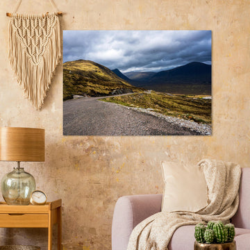 Glencoe Valley wall art showing a winding road from Glencoe Mountain Resort with golden hills, dark mountains and a dramatic cloudy sky over the Highland valley
