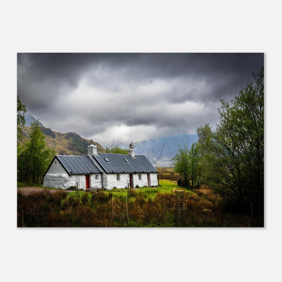 Blackrock Cottage Buachaille Etive Mòr wall art showing the white cottage in green moorland with trees and dramatic cloudy mountains in the Glencoe landscap