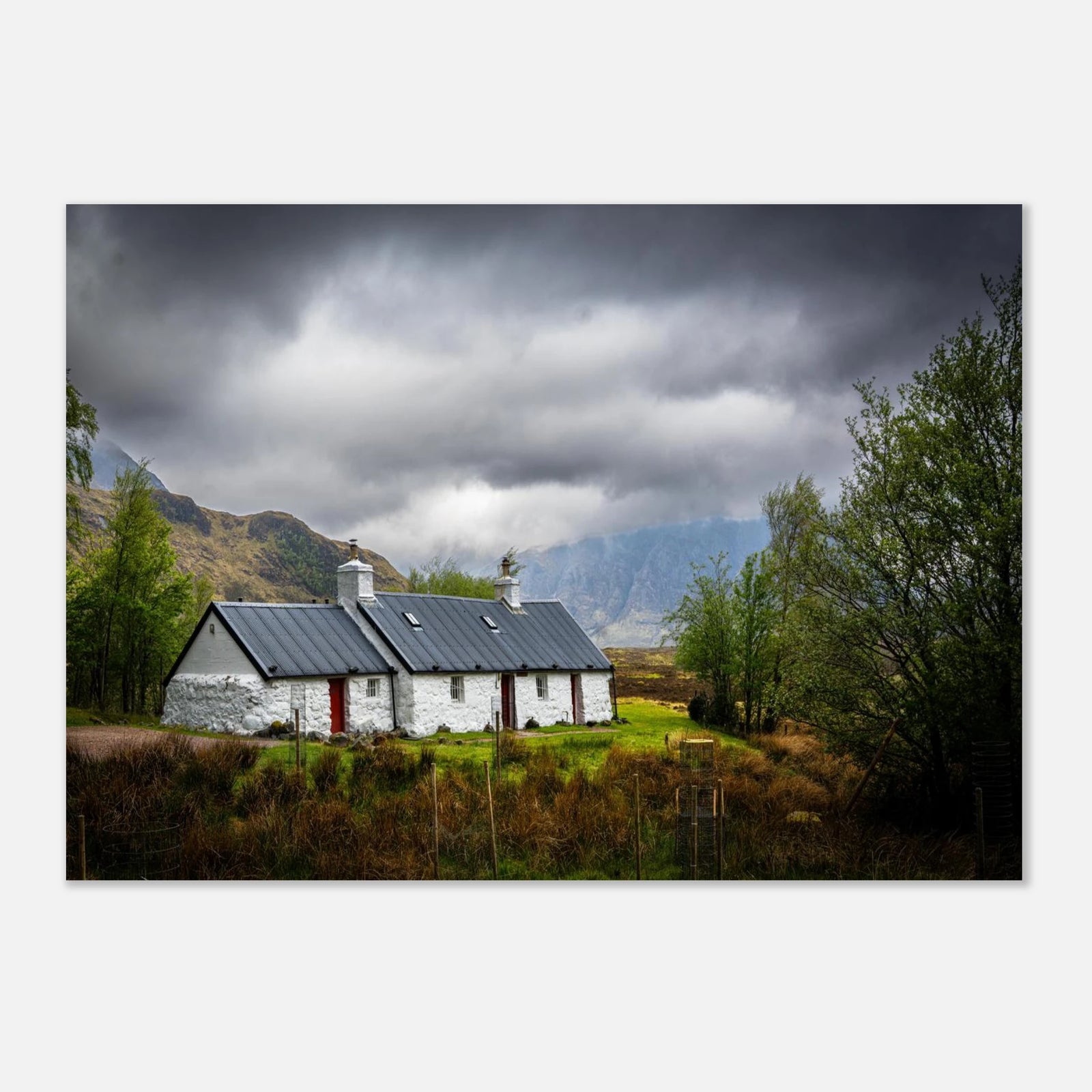 Blackrock Cottage Buachaille Etive Mòr wall art showing the white cottage in green moorland with trees and dramatic cloudy mountains in the Glencoe landscap