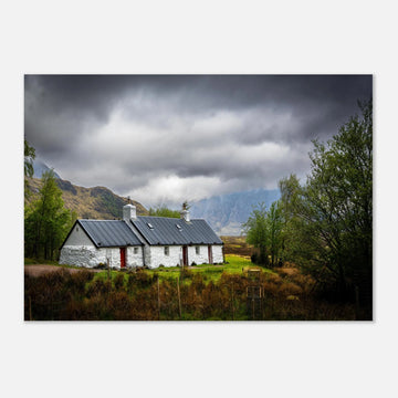 Blackrock Cottage Buachaille Etive Mòr wall art showing the white cottage in green moorland with trees and dramatic cloudy mountains in the Glencoe landscap
