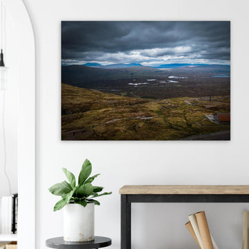 Glencoe Valley From Above wall art showing a wide Highland moor with distant blue hills, scattered lochans and heavy clouds over the Glencoe landscape