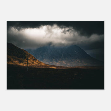 Glencoe sunrise wall art showing Buachaille Etive Mòr under dark storm clouds with a strip of warm light across the foreground moorland