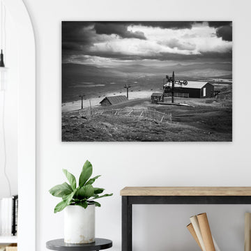 Glencoe Mountain View wall art showing a black and white panorama from Glencoe Mountain with ski lifts, small huts and a wide Highland landscape under dramatic clouds