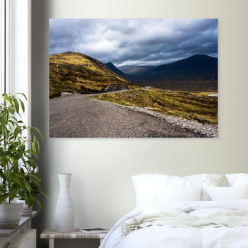 Glencoe Valley wall art showing a winding road from Glencoe Mountain Resort with golden hills, dark mountains and a dramatic cloudy sky over the Highland valley