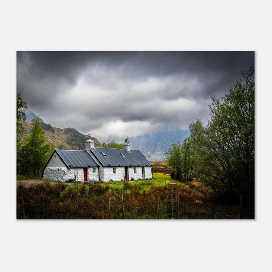 Blackrock Cottage Buachaille Etive Mòr wall art showing the white cottage in green moorland with trees and dramatic cloudy mountains in the Glencoe landscap