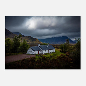 Blackrock Cottage Glencoe wall art showing a dark moody wide view of the white cottage surrounded by rough moorland and dramatic Scottish mountains under heavy clouds