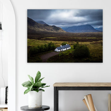 Blackrock Cottage Buachaille Etive Mòr wall art showing the white cottage in front of a dramatic Scottish Highlands mountain under dark storm clouds and moody light