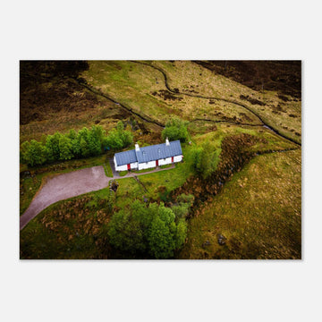 Blackrock Cottage Glencoe wall art showing an aerial view of the long white cottage with red doors surrounded by green moorland, trees and winding tracks