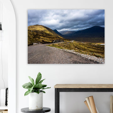 Glencoe Valley wall art showing a winding road from Glencoe Mountain Resort with golden hills, dark mountains and a dramatic cloudy sky over the Highland valley