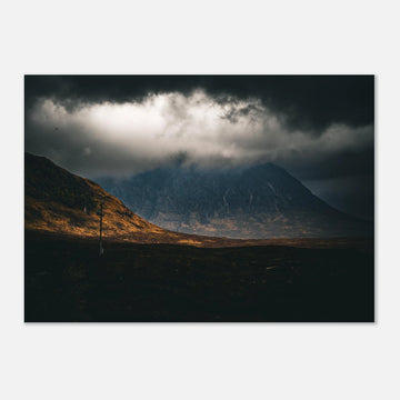 Glencoe sunrise wall art showing Buachaille Etive Mòr under dark storm clouds with a strip of warm light across the foreground moorland