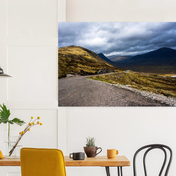 Glencoe Valley wall art showing a winding road from Glencoe Mountain Resort with golden hills, dark mountains and a dramatic cloudy sky over the Highland valley