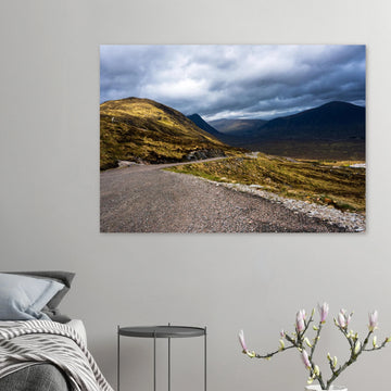 Glencoe Valley wall art showing a winding road from Glencoe Mountain Resort with golden hills, dark mountains and a dramatic cloudy sky over the Highland valley