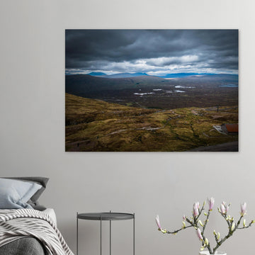 Glencoe Valley From Above wall art showing a wide Highland moor with distant blue hills, scattered lochans and heavy clouds over the Glencoe landscape