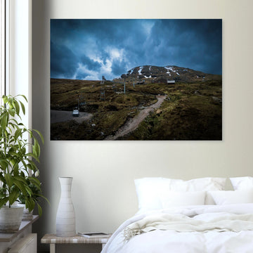 Glencoe Ski Lift wall art showing empty chairlifts climbing a rugged hillside towards snow patches with dramatic blue-grey clouds over Glencoe Mountain Resort