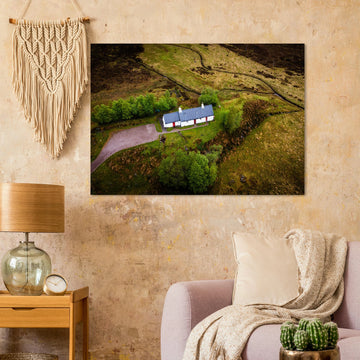 Blackrock Cottage Glencoe wall art showing an aerial view of the long white cottage with red doors surrounded by green moorland, trees and winding tracks