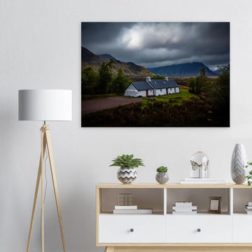Blackrock Cottage Glencoe wall art showing a dark moody wide view of the white cottage surrounded by rough moorland and dramatic Scottish mountains under heavy clouds