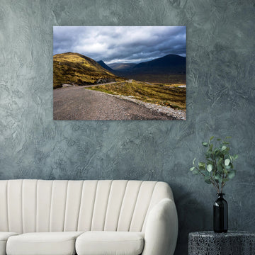 Glencoe Valley wall art showing a winding road from Glencoe Mountain Resort with golden hills, dark mountains and a dramatic cloudy sky over the Highland valley