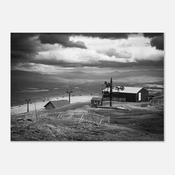 Glencoe Mountain View wall art showing a black and white panorama from Glencoe Mountain with ski lifts, small huts and a wide Highland landscape under dramatic clouds