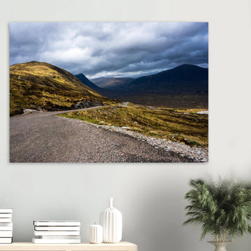 Glencoe Valley wall art showing a winding road from Glencoe Mountain Resort with golden hills, dark mountains and a dramatic cloudy sky over the Highland valley