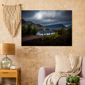 Blackrock Cottage Glencoe wall art showing a dark moody wide view of the white cottage surrounded by rough moorland and dramatic Scottish mountains under heavy clouds