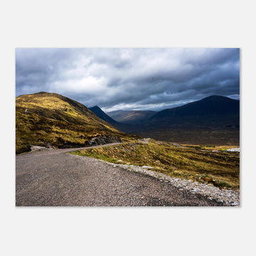 Glencoe Valley wall art showing a winding road from Glencoe Mountain Resort with golden hills, dark mountains and a dramatic cloudy sky over the Highland valley