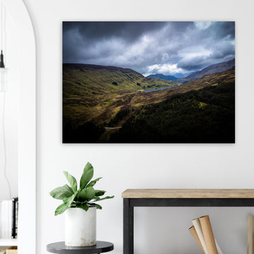 Scottish Highlands Glen wall art showing a rugged valley with rolling heather hills, a small loch and heavy storm clouds over the remote Scottish landscape