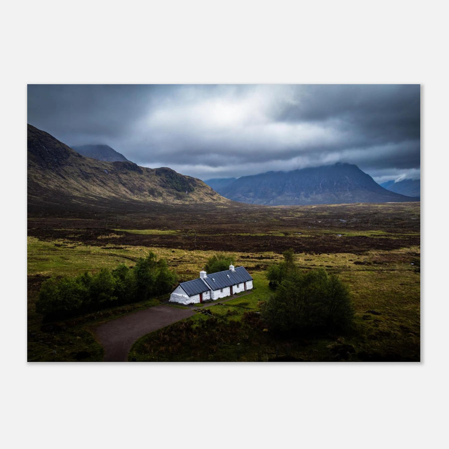 Blackrock Cottage Buachaille Etive Mòr wall art showing the white cottage in front of a dramatic Scottish Highlands mountain under dark storm clouds and moody light