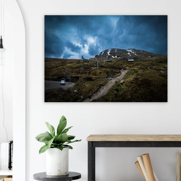 Glencoe Ski Lift wall art showing empty chairlifts climbing a rugged hillside towards snow patches with dramatic blue-grey clouds over Glencoe Mountain Resort