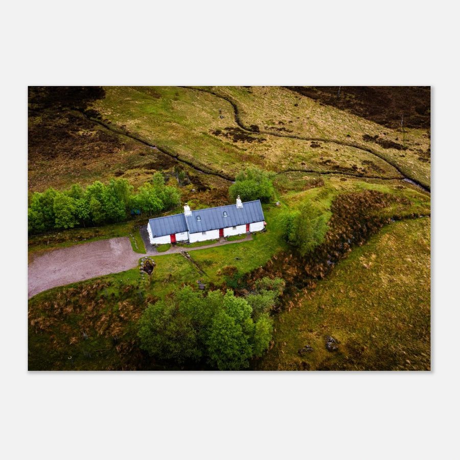 Blackrock Cottage Glencoe wall art showing an aerial view of the long white cottage with red doors surrounded by green moorland, trees and winding tracks
