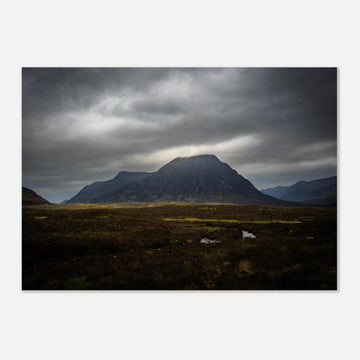 Buachaille Etive Mòr stormy sunrise wall art showing the dark Glencoe mountain under heavy clouds with a strip of light over the foreground moorland