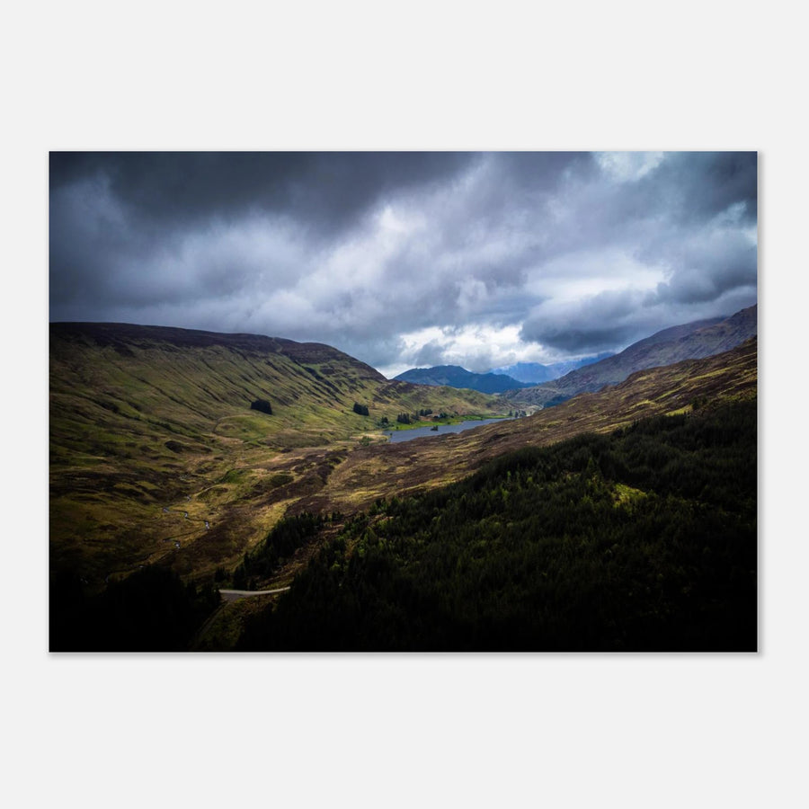 Scottish Highlands Glen wall art showing a rugged valley with rolling heather hills, a small loch and heavy storm clouds over the remote Scottish landscape