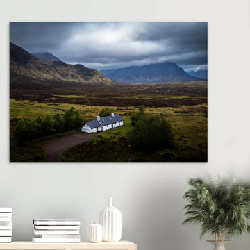 Blackrock Cottage Buachaille Etive Mòr wall art showing the white cottage in front of a dramatic Scottish Highlands mountain under dark storm clouds and moody light