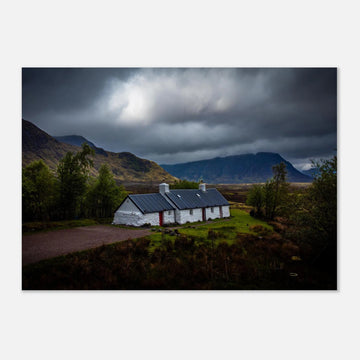 Blackrock Cottage Glencoe wall art showing a dark moody wide view of the white cottage surrounded by rough moorland and dramatic Scottish mountains under heavy clouds